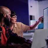 Two people collaborating at a computer, pointing at a monitor in an office setting