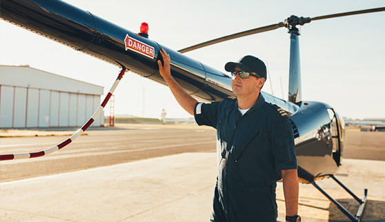 Male pilot in uniform examining helicopter tail wing. Pre flight inspection by pilot at the airport. 