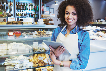 Smiling young woman holding a tablet in a bakery