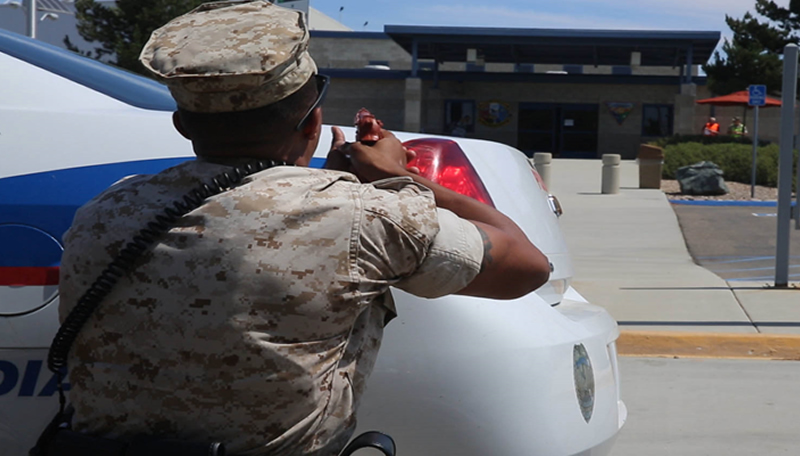 A student seeks cover behind a police vehicle during a training exercise