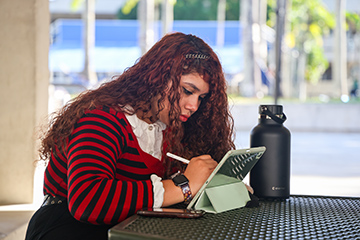 Student working on a tablet at one of the campus tables