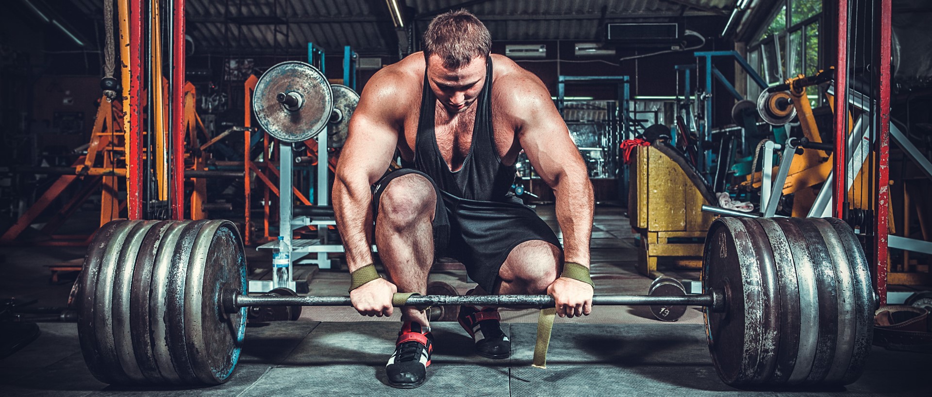 A muscular man prepares to dead lift a large amount of weights