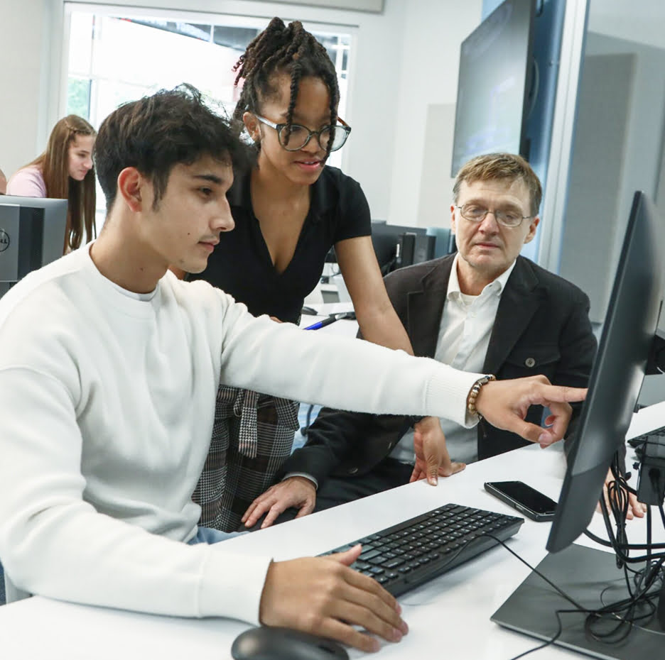 Students and a professor working together at a computer in a classroom.