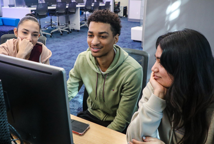 Three students in a computer lab, looking a a screen.