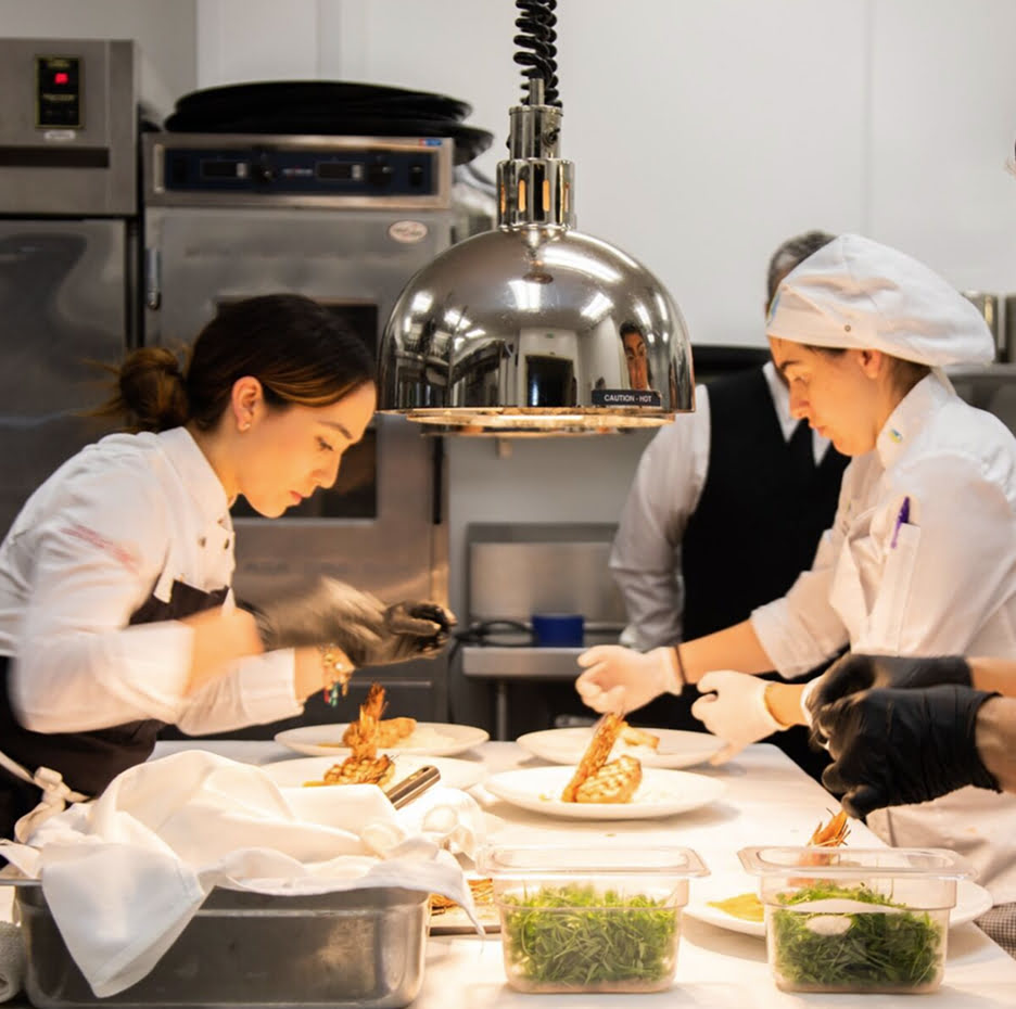 Culinary students plating food in a professional kitchen.
