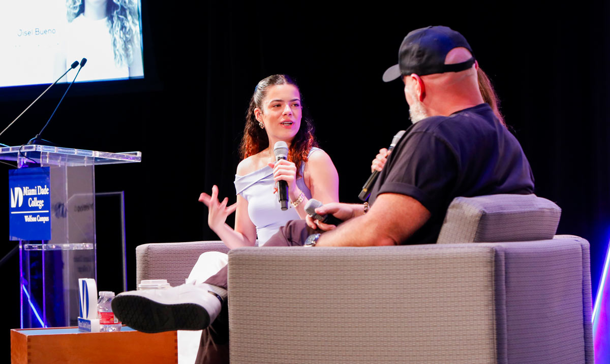 A man and a woman engage in a panel discussion on stage at Miami Dade College.
