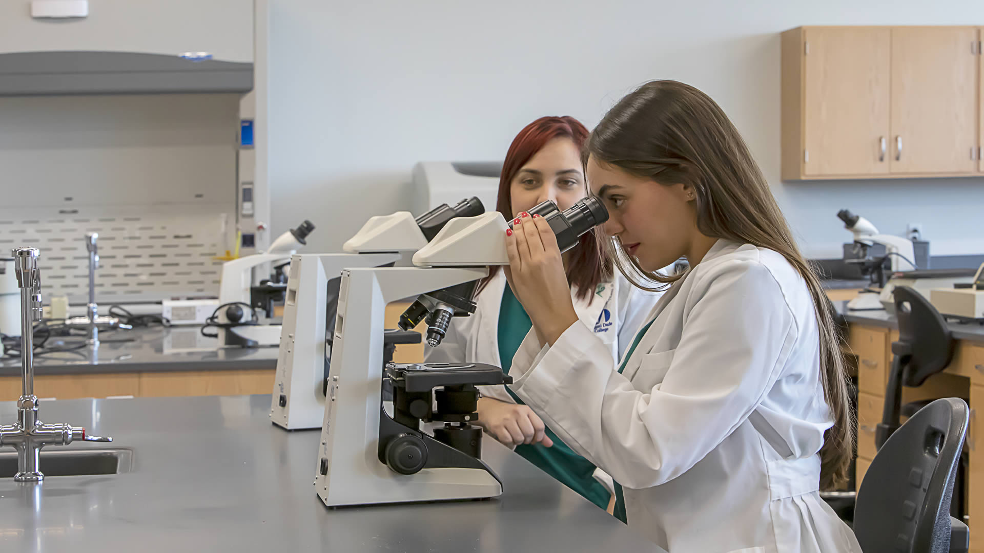 Two medical students study slides under a microscope in a lab