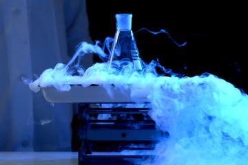 A beaker undergoes a chemical reaction in subdued blue light