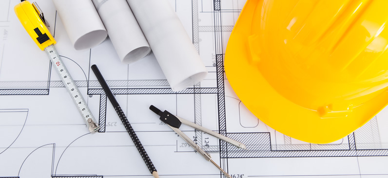 Blueprint placed on a table with a yellow hard hat, pencil and compass