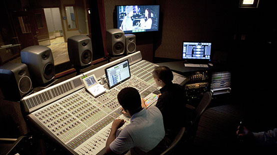 Two students sitting in front of Music studio and production console