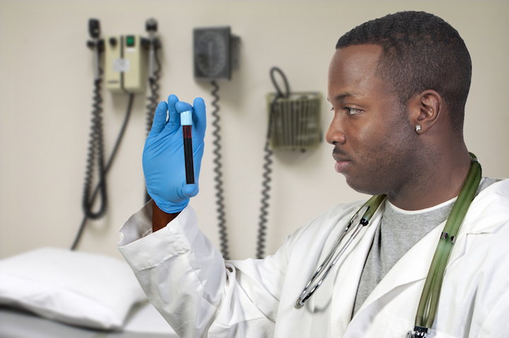 Male phlebotomist looks at a vial of blood.