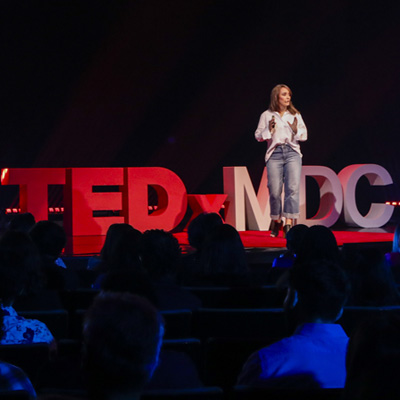 A speaker on stage in front of a TedxMDc sign